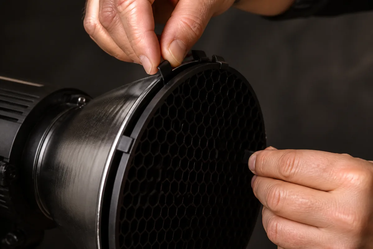 Mains ajustant une grille en nid d’abeille sur un projecteur de studio