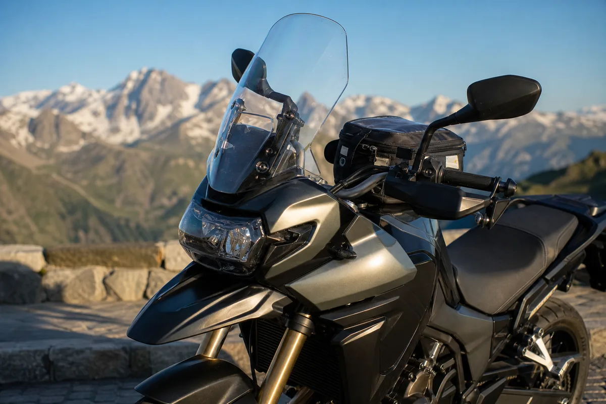 Moto de voyage vue de profil avant garée face à un panorama de sommets alpins